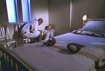 Buffy's hospital room as described. Bed with restraints in foreground; Buffy sits in the corner on the floor, with the doctor on a  chair talking to her